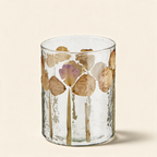 Glass votive with real flower petals set into the glass on a warm cream background