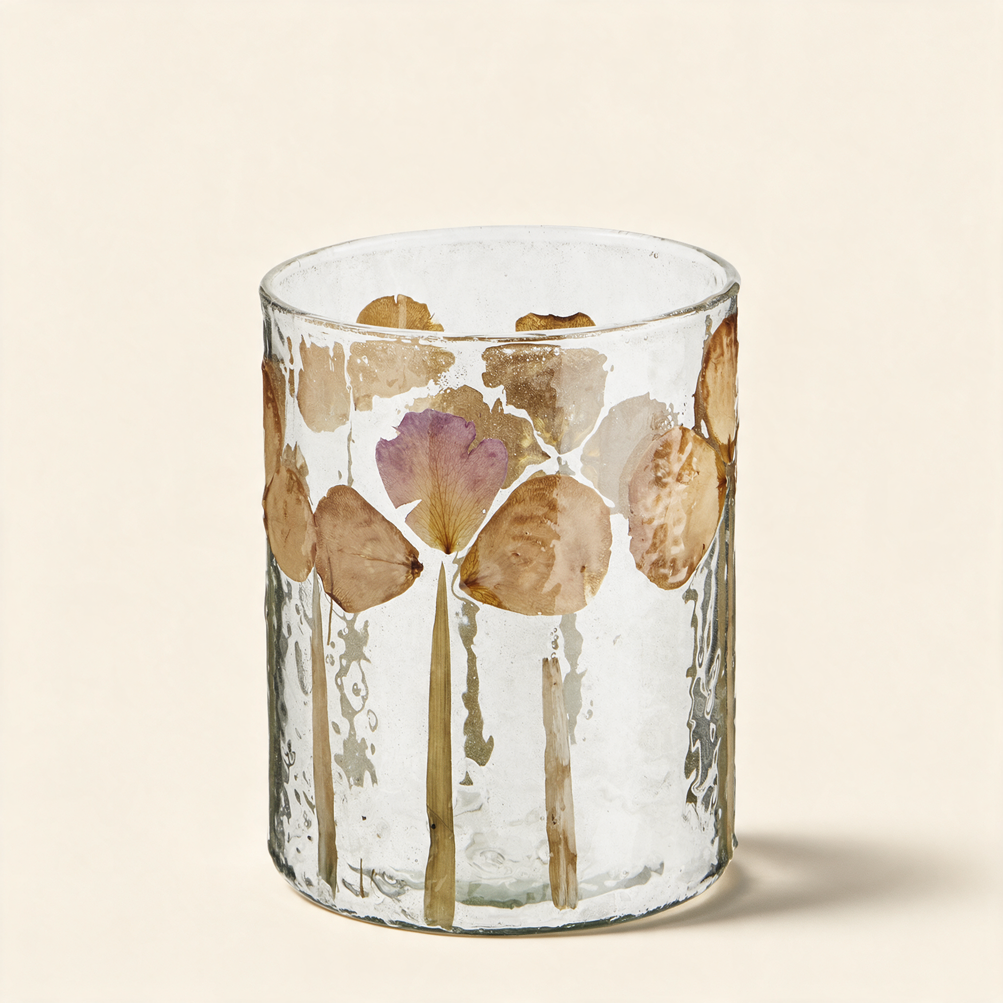 Glass votive with real flower petals set into the glass on a warm cream background