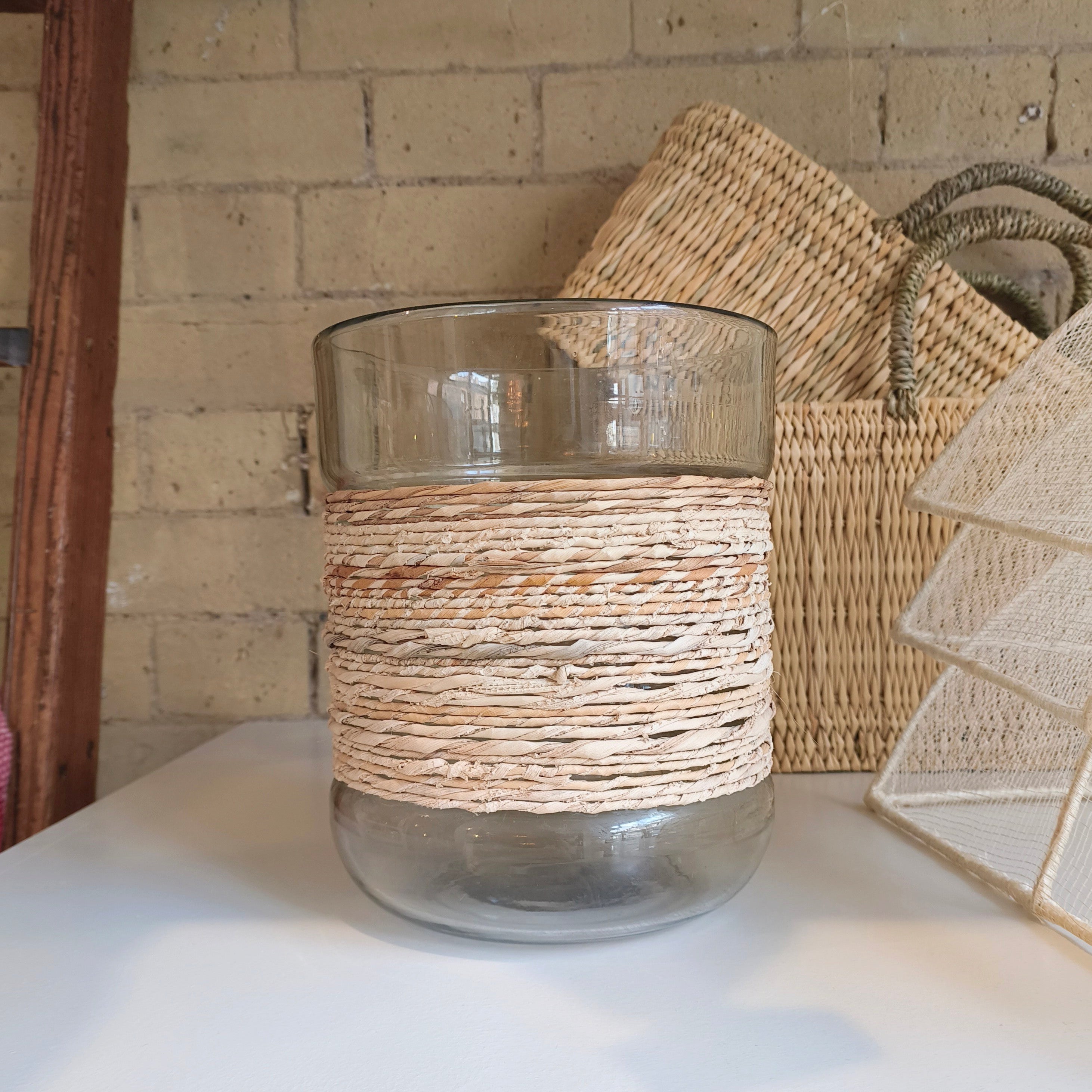 Clear glass vase with woven brown top on a white surface