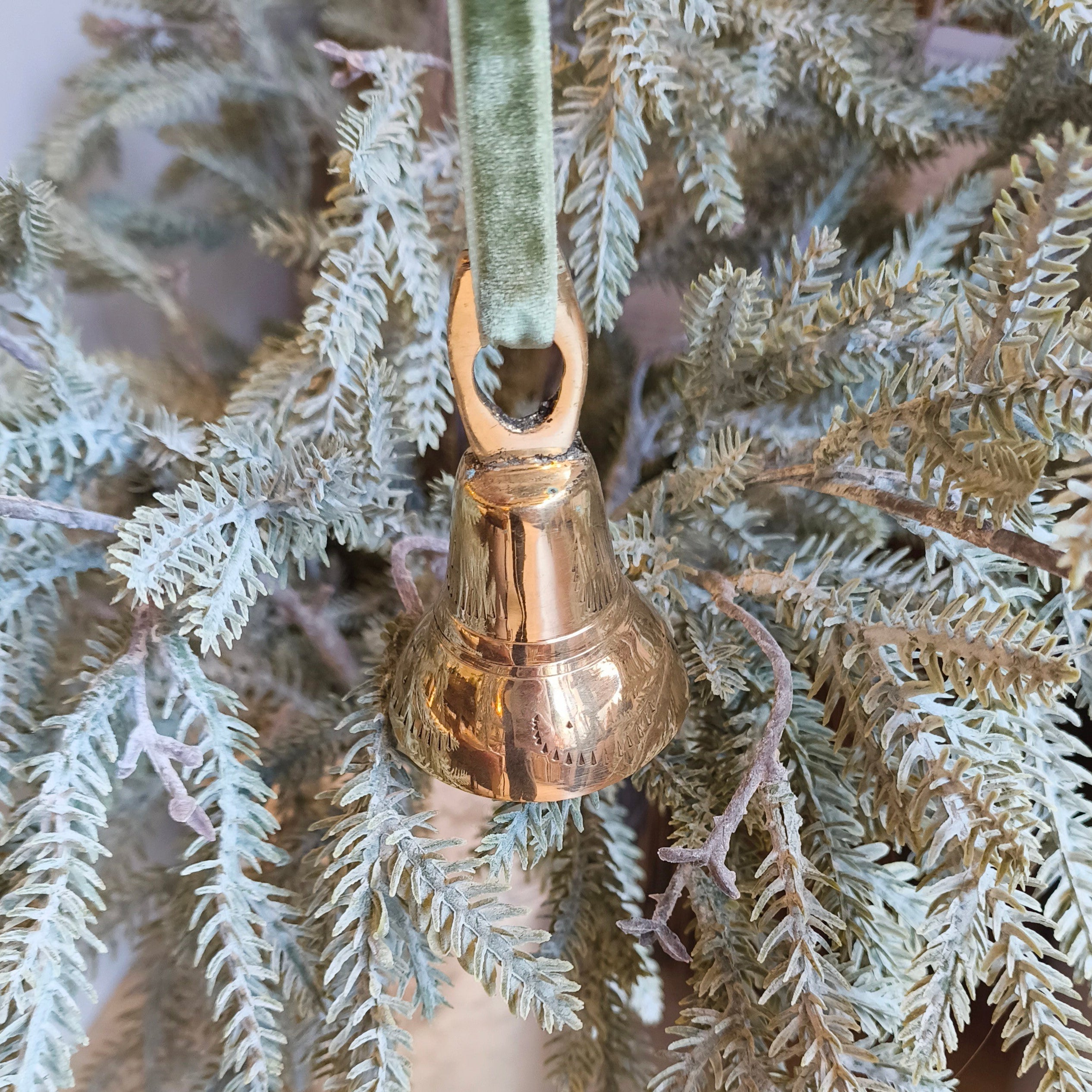 Decorative gold bell hanging from a branch of a Christmas tree.