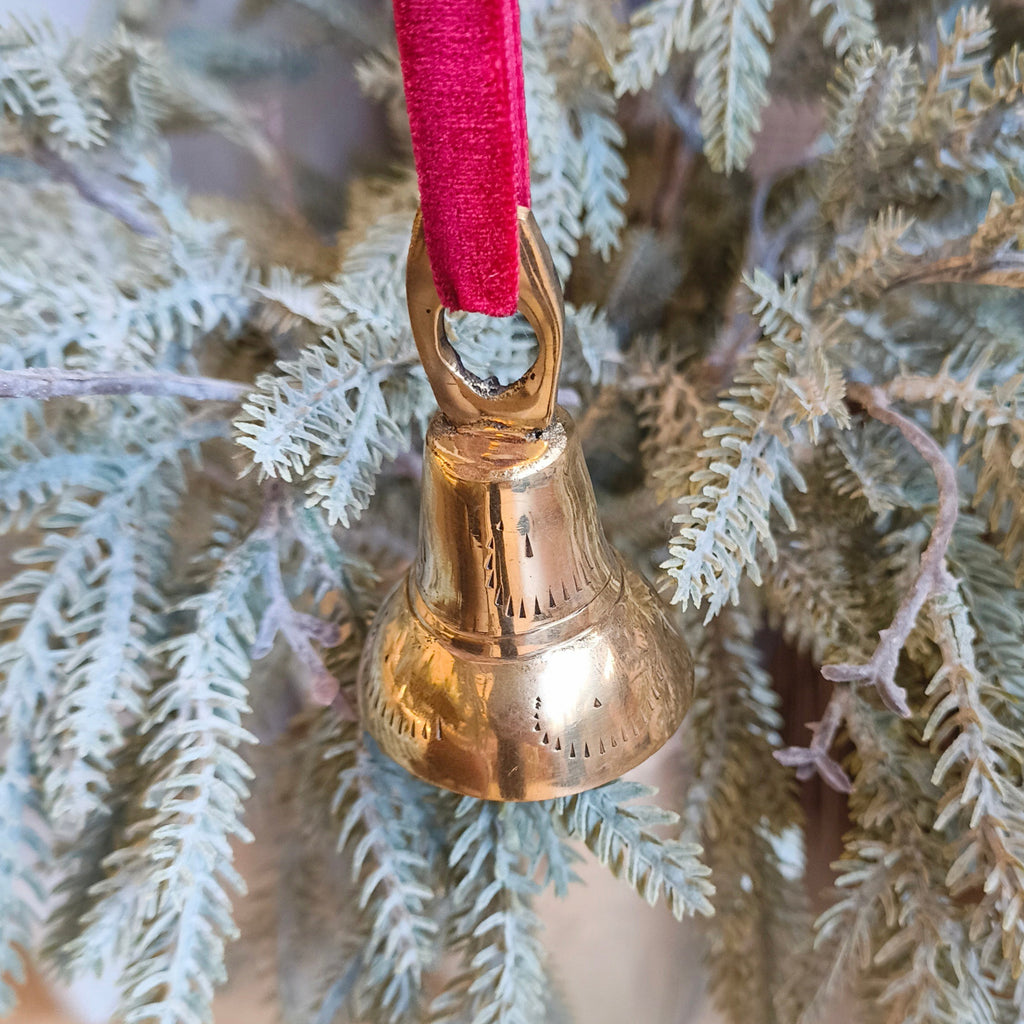 Gold bell ornament with red ribbon on a branch of a Christmas tree.