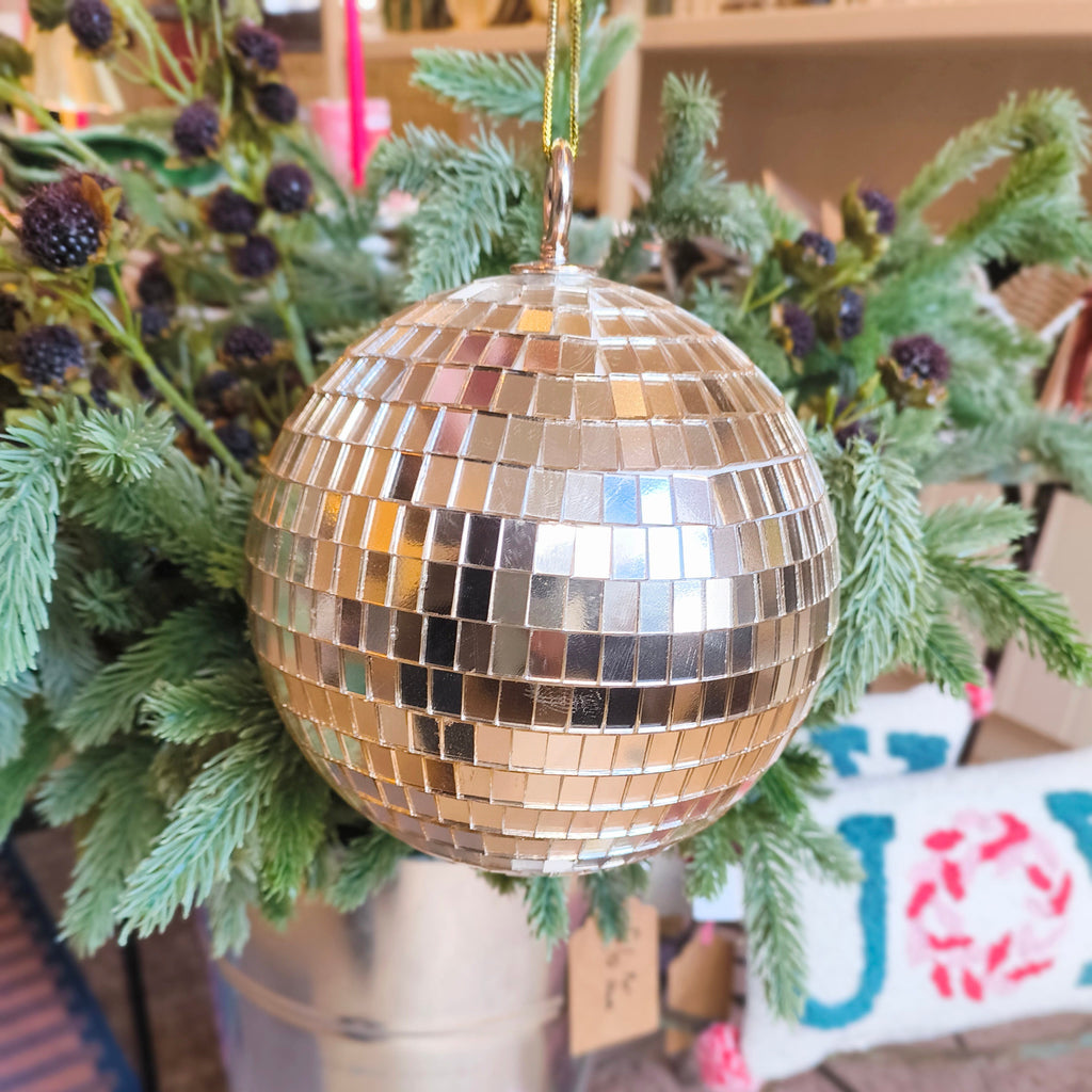 Gold disco ball ornament on a Christmas tree with greenery and decorations.
