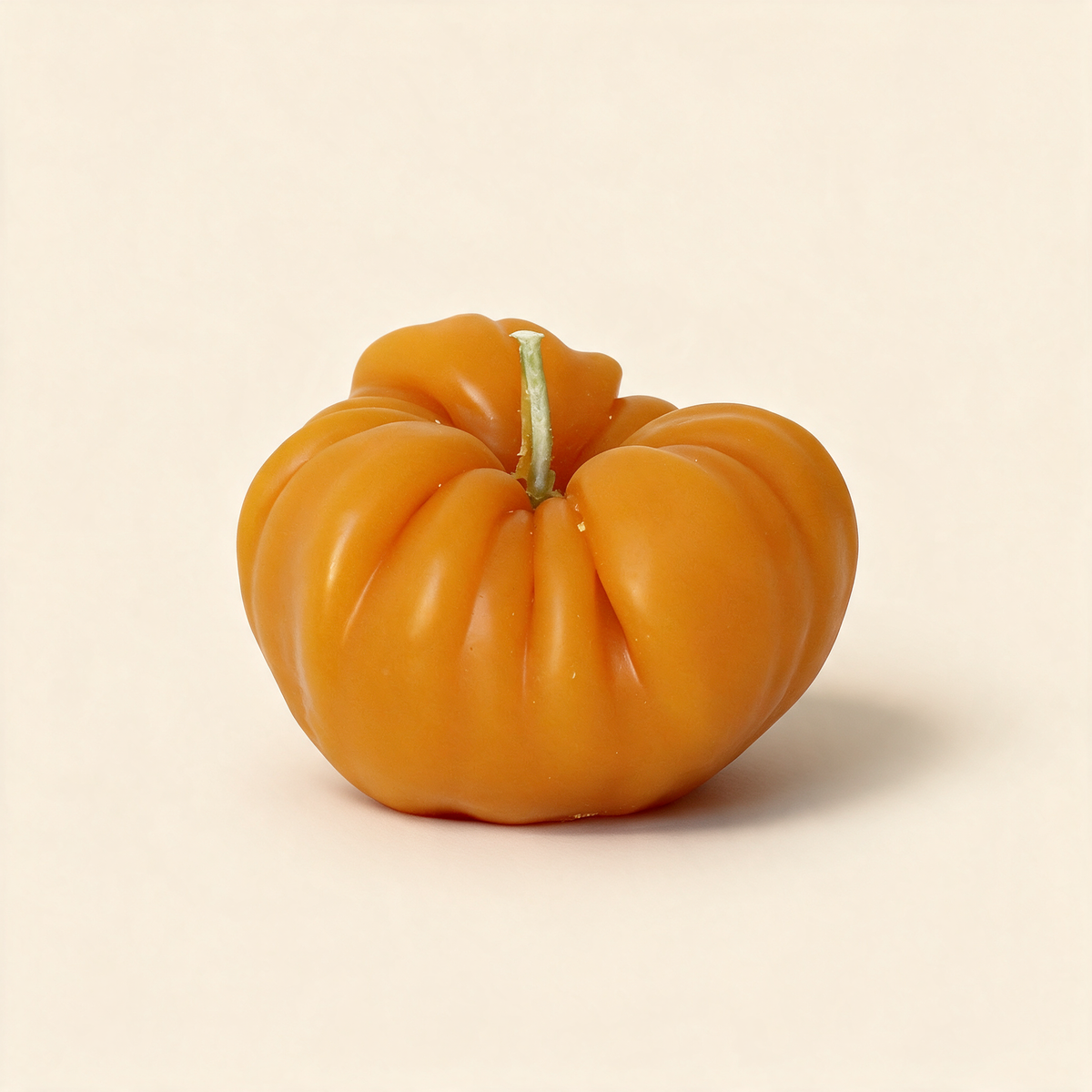 Golden heirloom tomato-shaped beeswax candle on a cream background