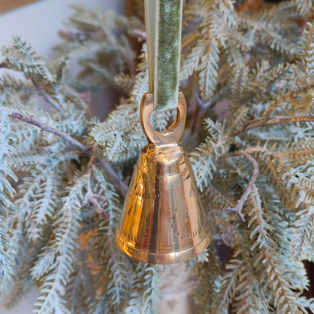 Bronze bell ornament hanging on a branch with a green velvet ribbon.