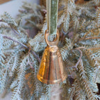 Bronze bell ornament hanging on a branch with a green velvet ribbon.