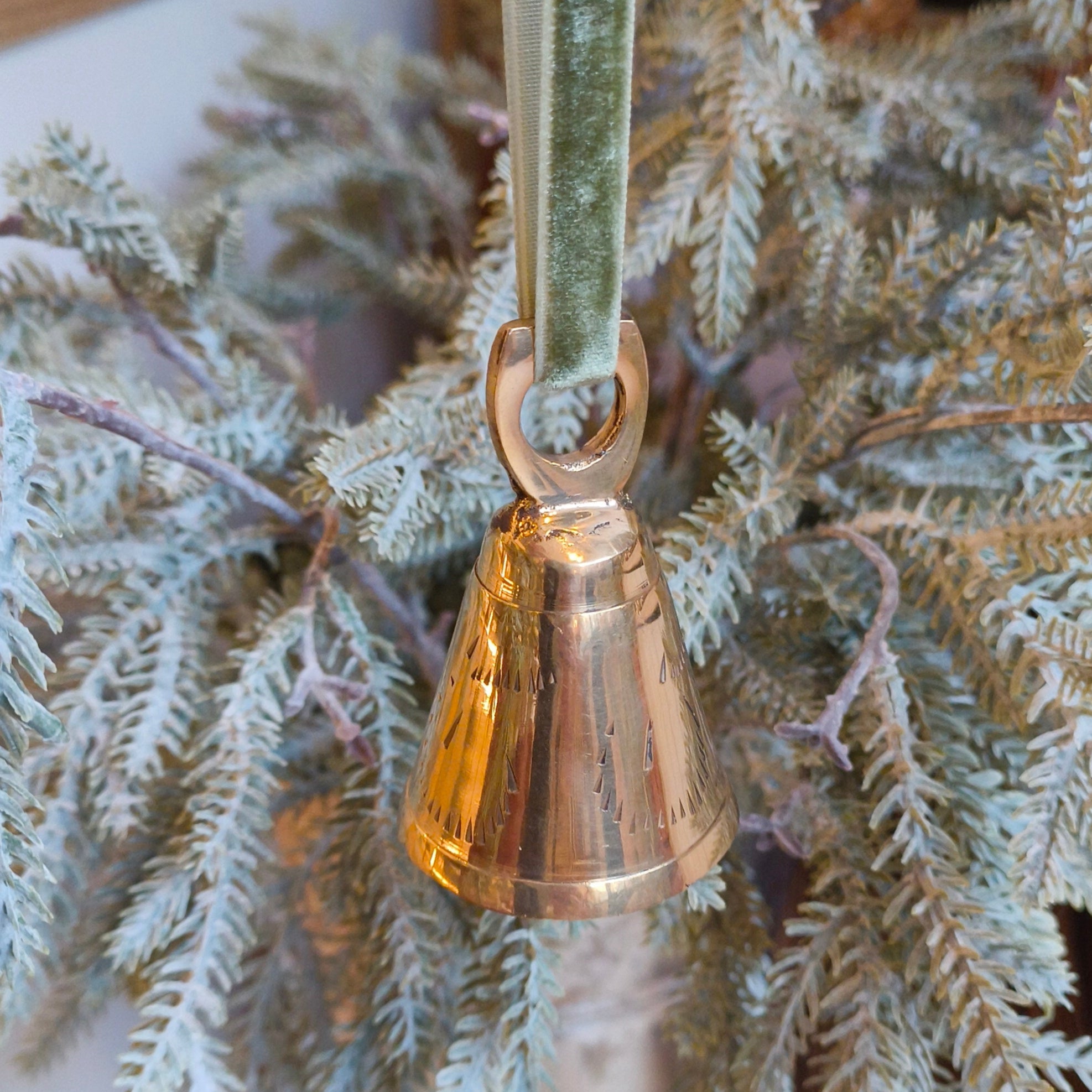 Bronze bell ornament hanging on a branch with a green velvet ribbon.