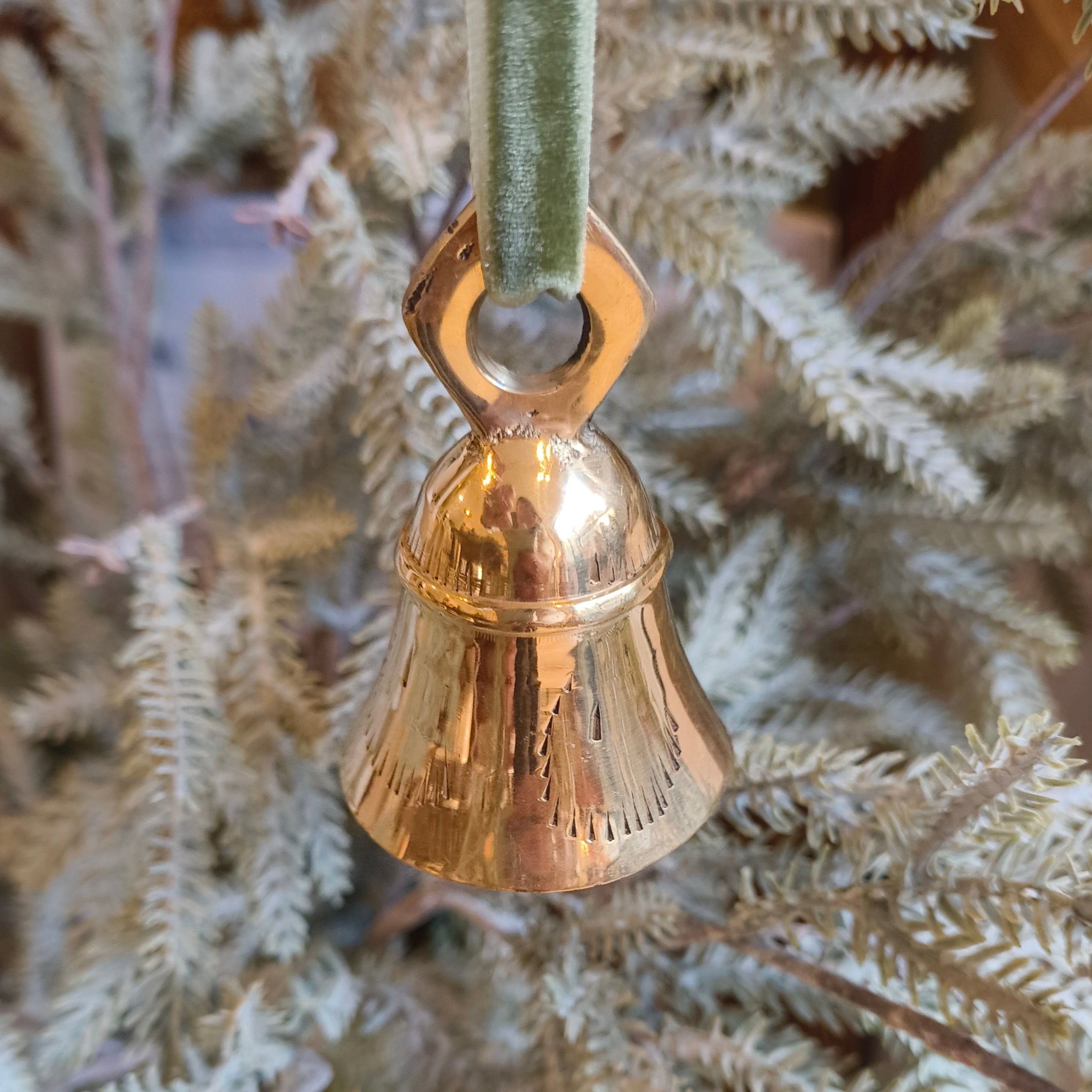 Gold bell ornament hanging on a branch of a decorated tree