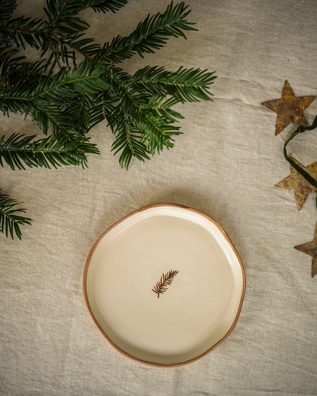 Hand painted pine snack plate with a green pine sprig, styled with festive greenery