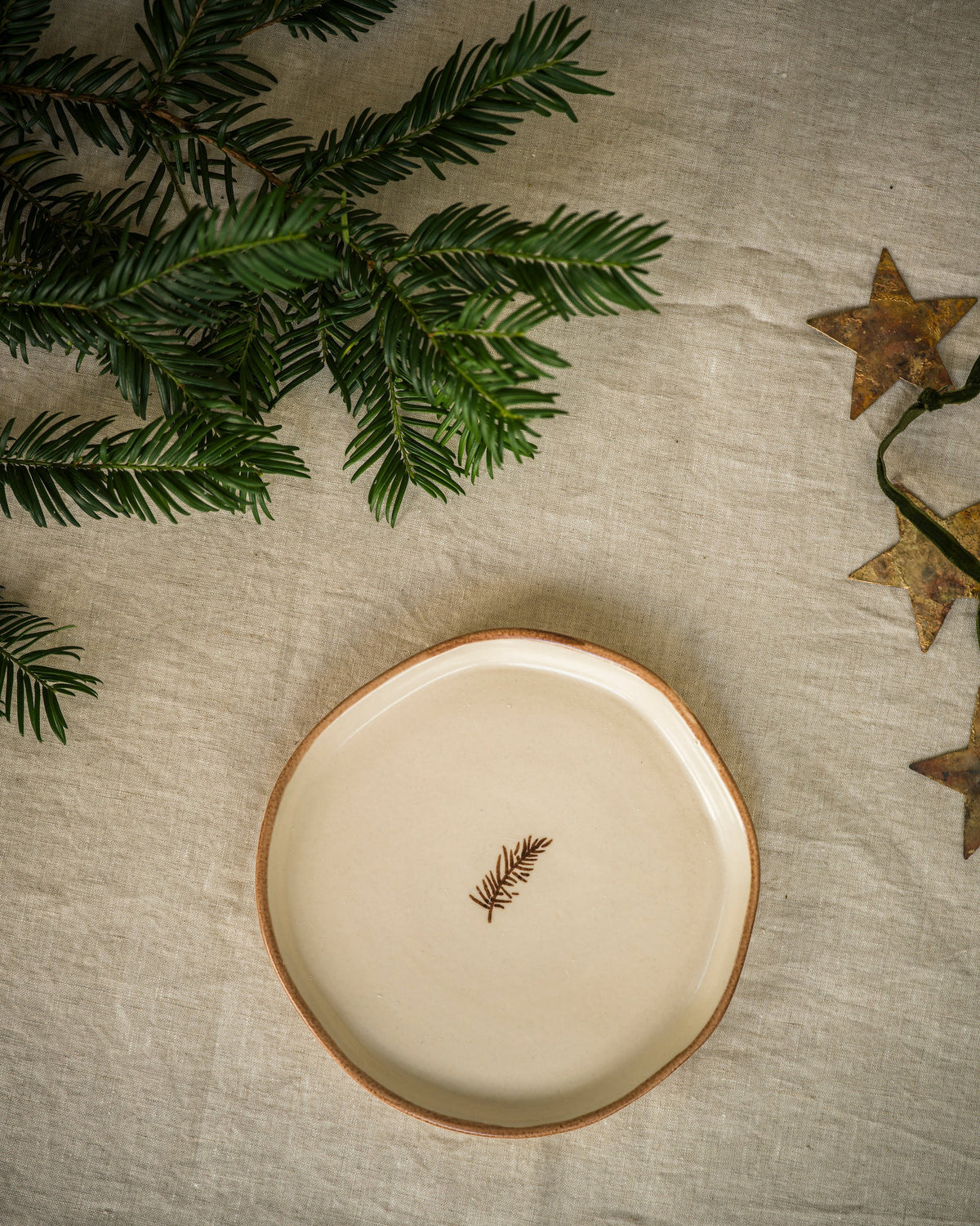 Hand painted pine snack plate with a green pine sprig, styled with festive greenery
