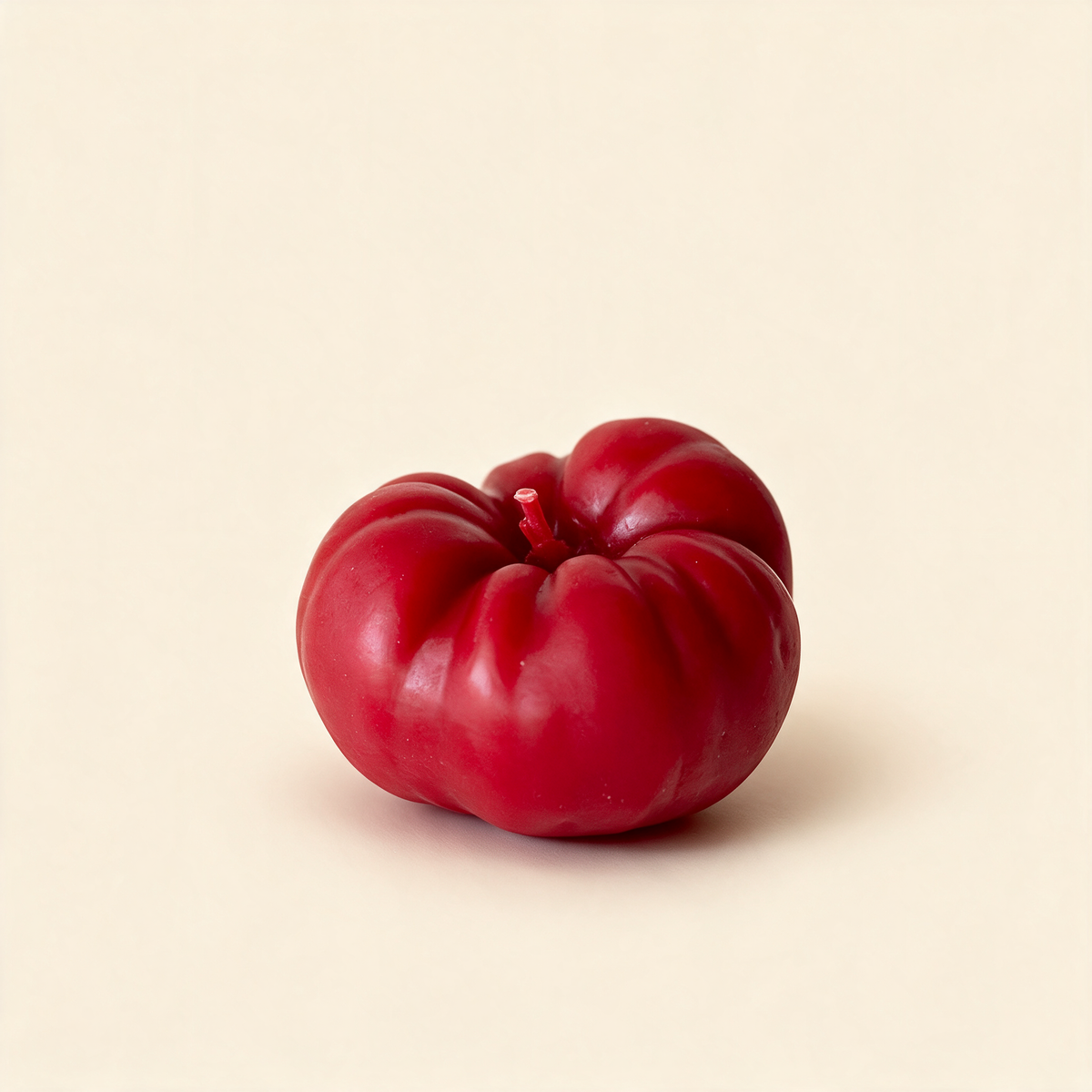 Heirloom tomato-shaped beeswax candle on a cream background