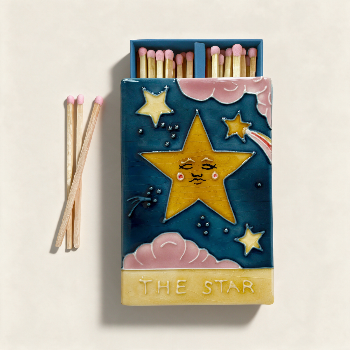 Ceramic match box with hand-glazed tarot 'The Star' lid, deep blue sky and golden star, holding coloured extra-long matches, on a cream background