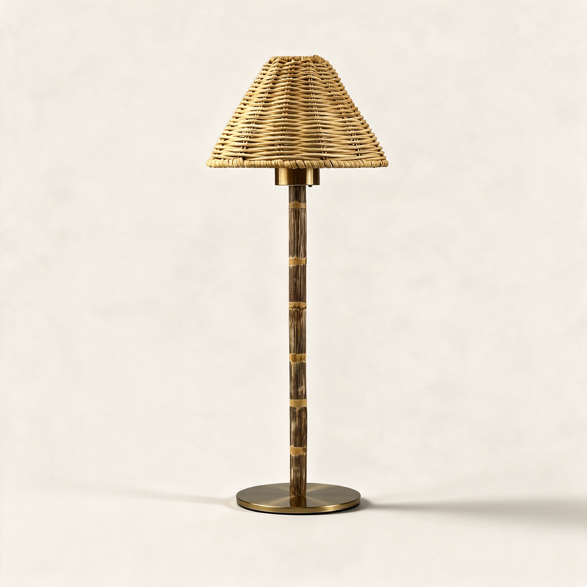 Cordless table lamp with a wicker shade and engraved metal base on a cream background