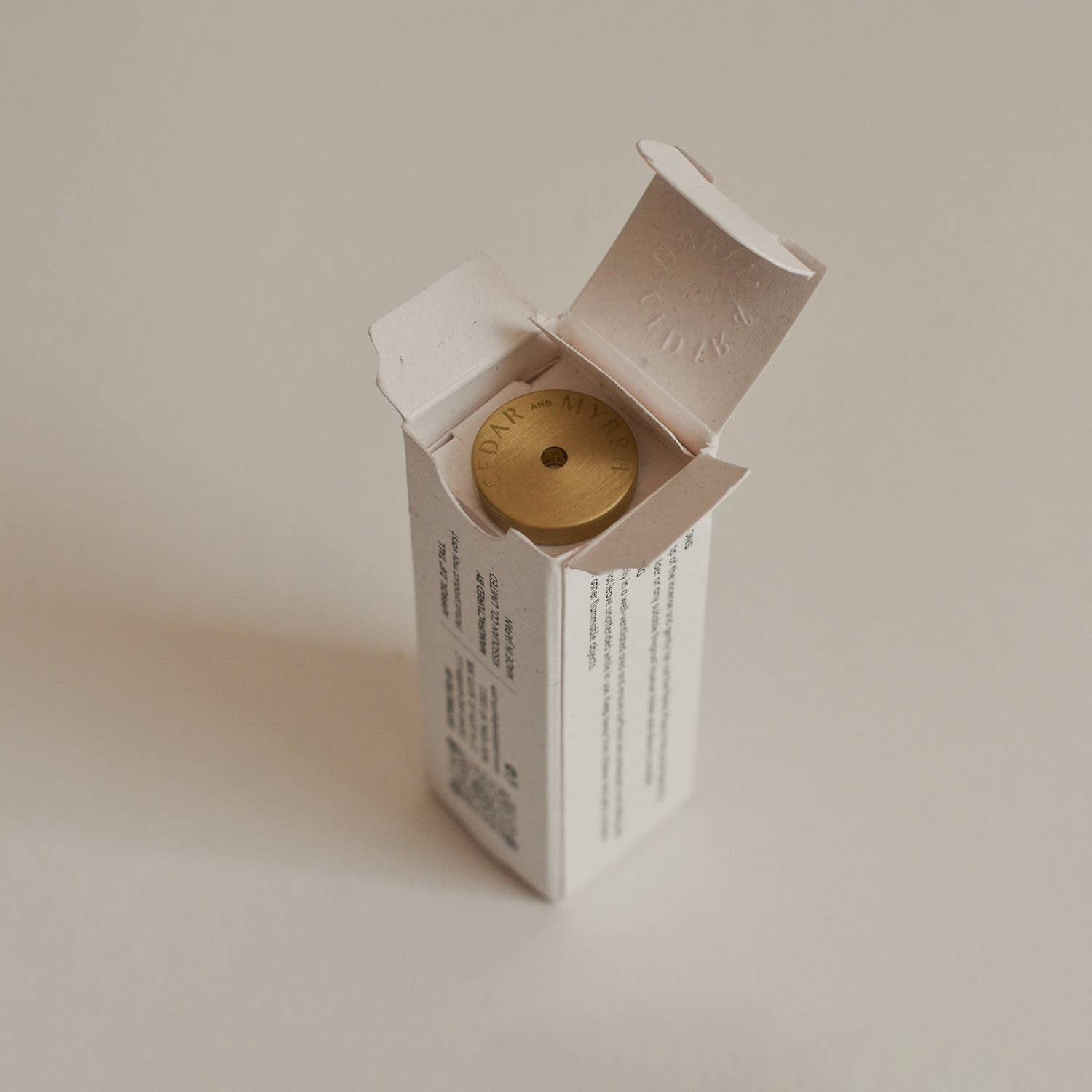 Small white box with a gold circular object inside on a beige background