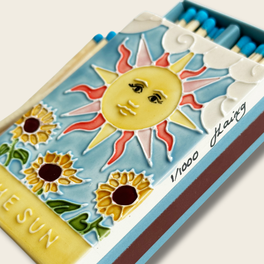 Decorative matchbox with sun and sunflower design on a white background