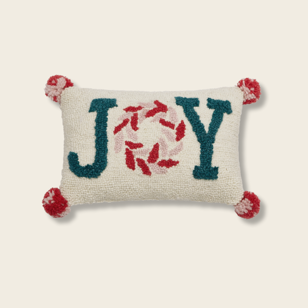Decorative pillow with 'JOY' text and pom-pom details on a beige background