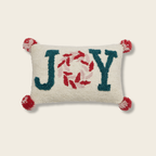 Decorative pillow with 'JOY' text and pom-pom details on a beige background