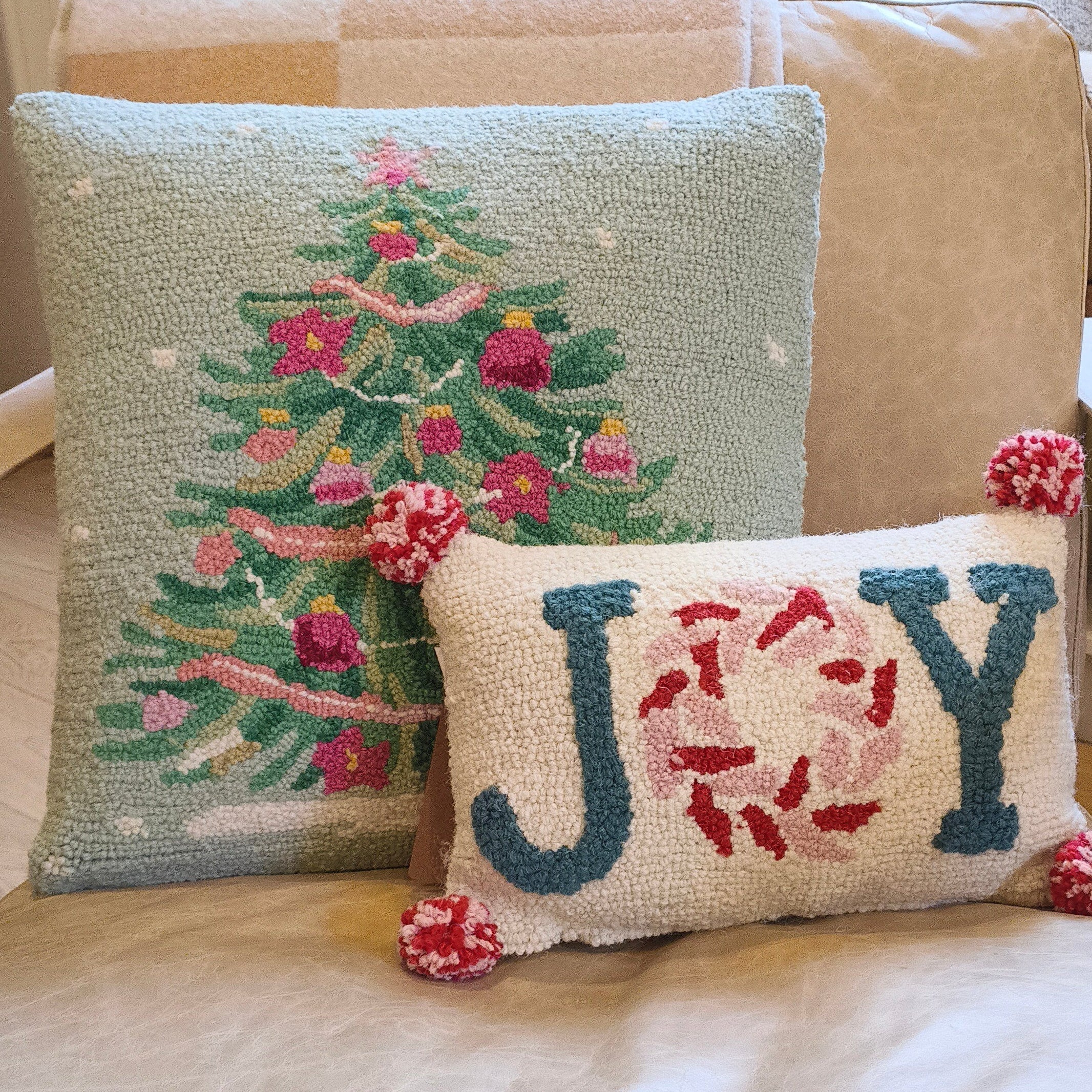 Decorative pillows on a beige couch with a Christmas tree and 'JOY' design.