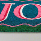 Close-up of a doormat with pink and blue text on a green background