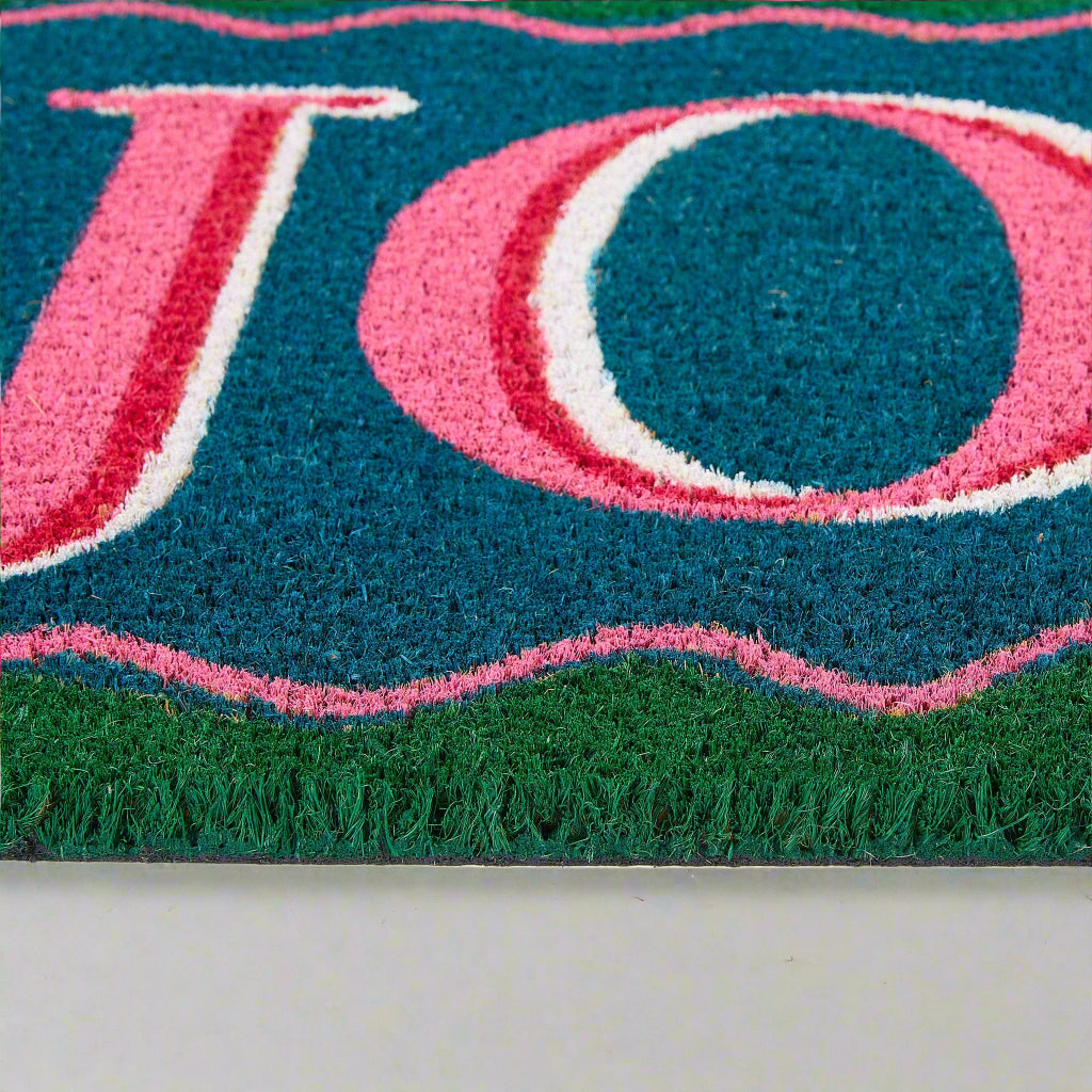 Close-up of a doormat with pink and blue text on a green background
