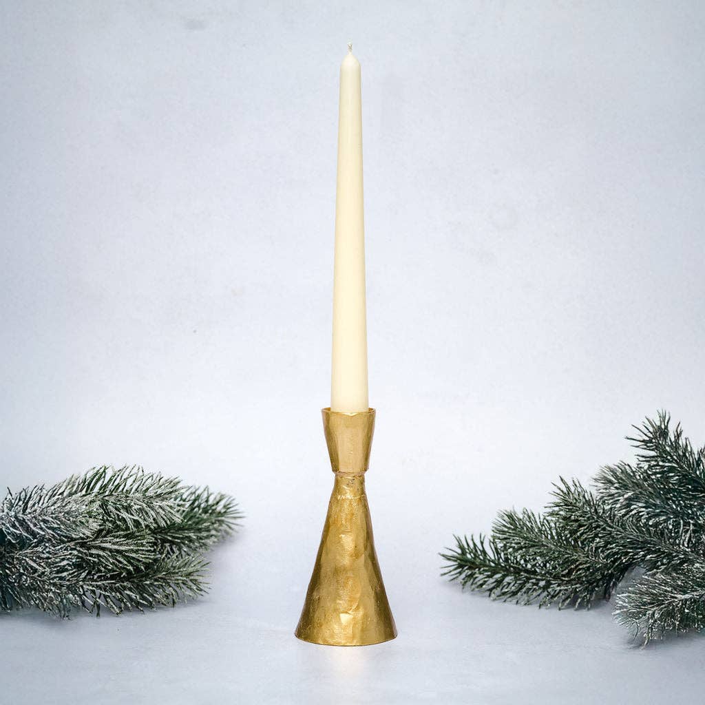 Gold candle holder with a white candle on a light gray background with decorative greenery.