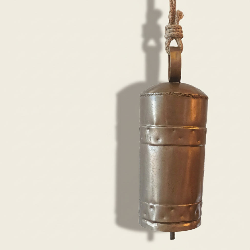 Metal bell hanging against a textured white brick wall