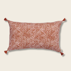 A square-shaped cushion cover with a leopard print pattern on a terracotta background, featuring small tassels on the corners.