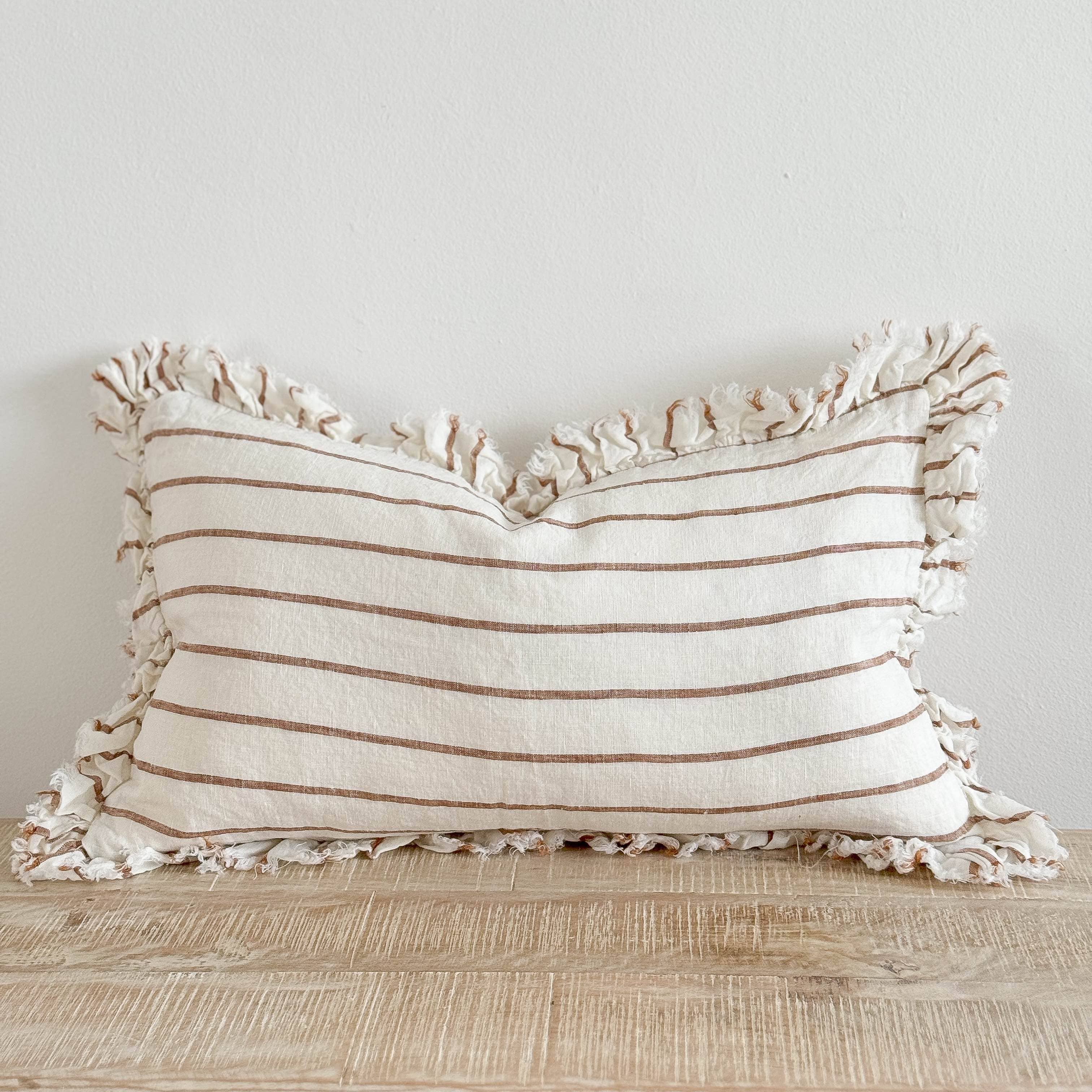 Striped pillow with ruffled edges on a wooden surface against a light background