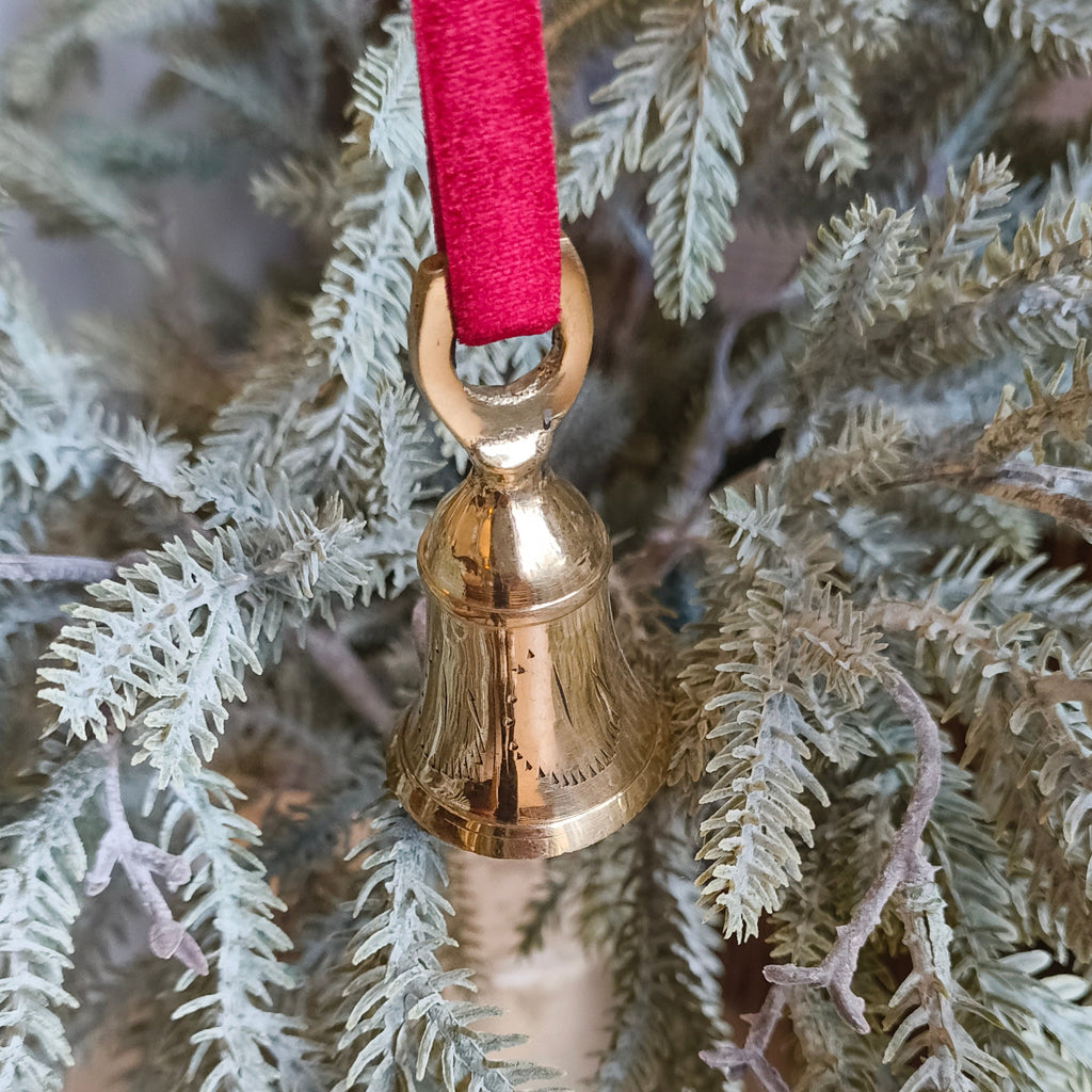 Gold bell ornament on a branch with a red ribbon against a wooden background