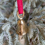 Gold bell ornament on a branch with a red ribbon against a wooden background