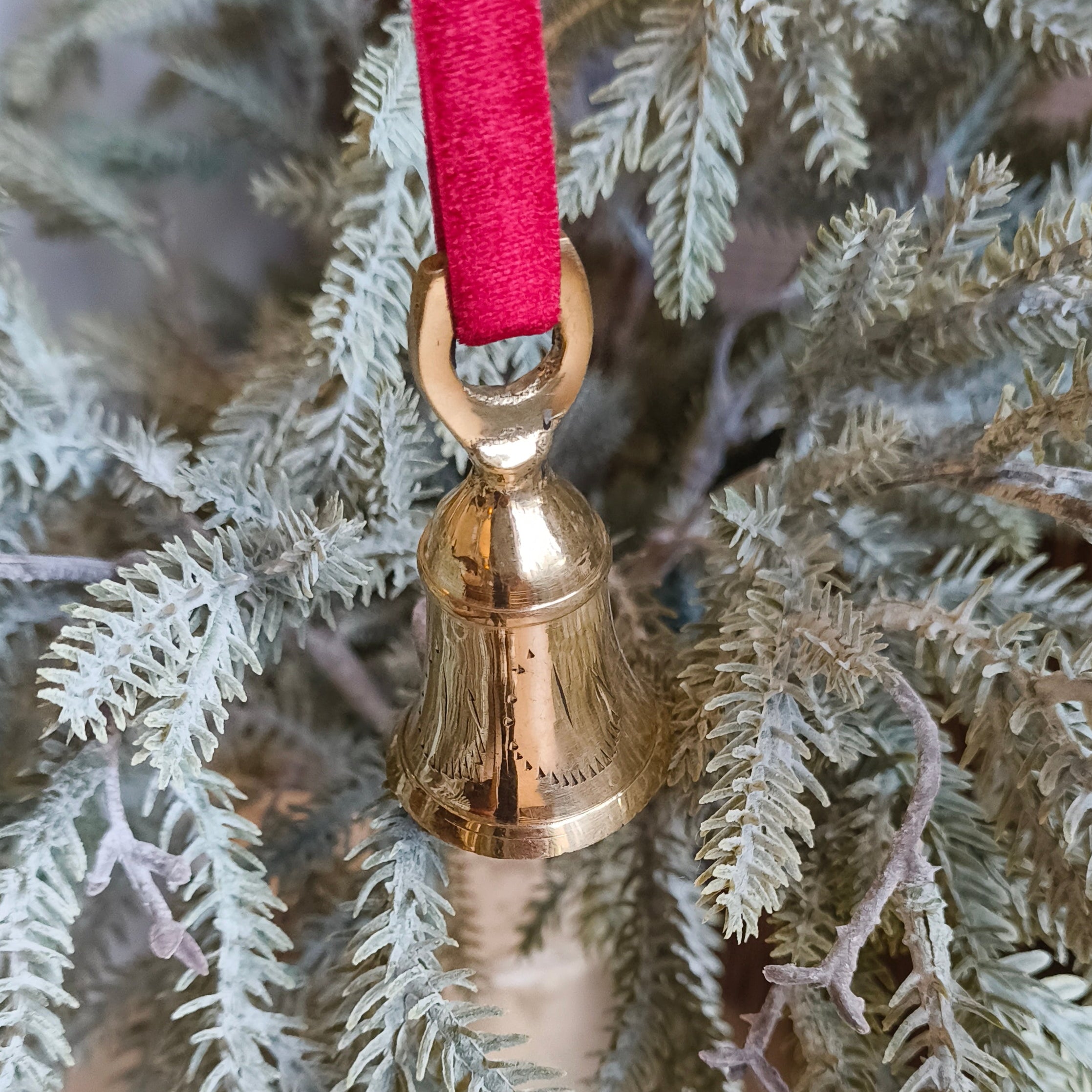 Gold bell ornament on a branch with a red ribbon against a wooden background