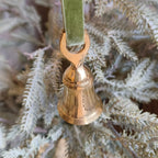 Gold bell ornament on a green ribbon hanging on a Christmas tree.