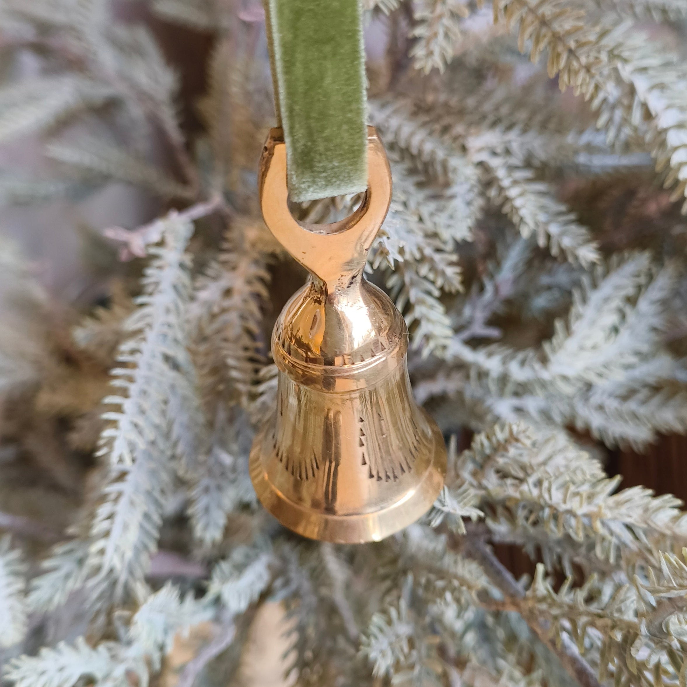 Gold bell ornament on a green ribbon hanging on a Christmas tree.
