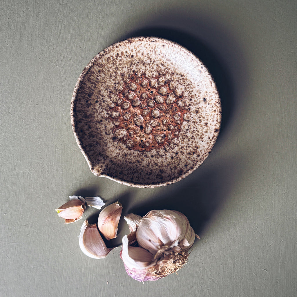 Speckled ceramic bowl with garlic cloves on a gray background