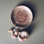 Speckled ceramic bowl with garlic cloves on a gray background
