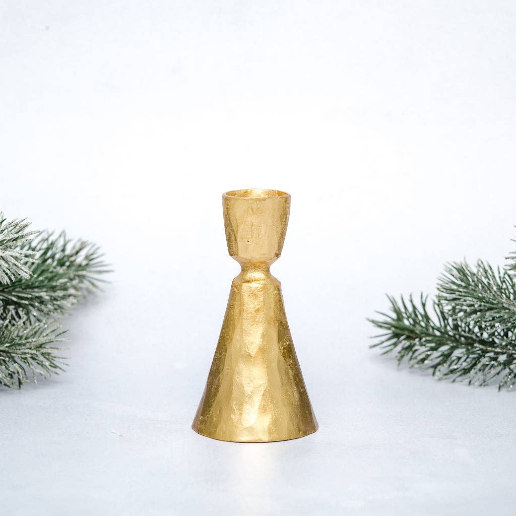 Gold bell-shaped candle holder with greenery on a white background