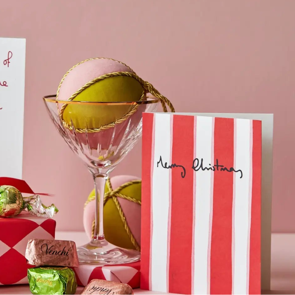 Christmas-themed gift set with a card, candy, and decorative items on a pink background