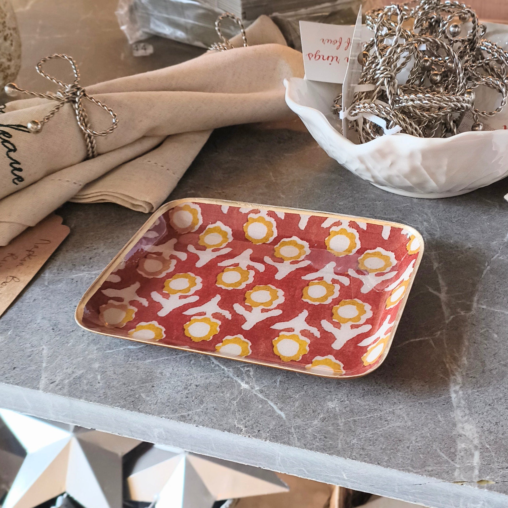 Tabletop display with decorative items including a red patterned tray, a pink container, and a green book.