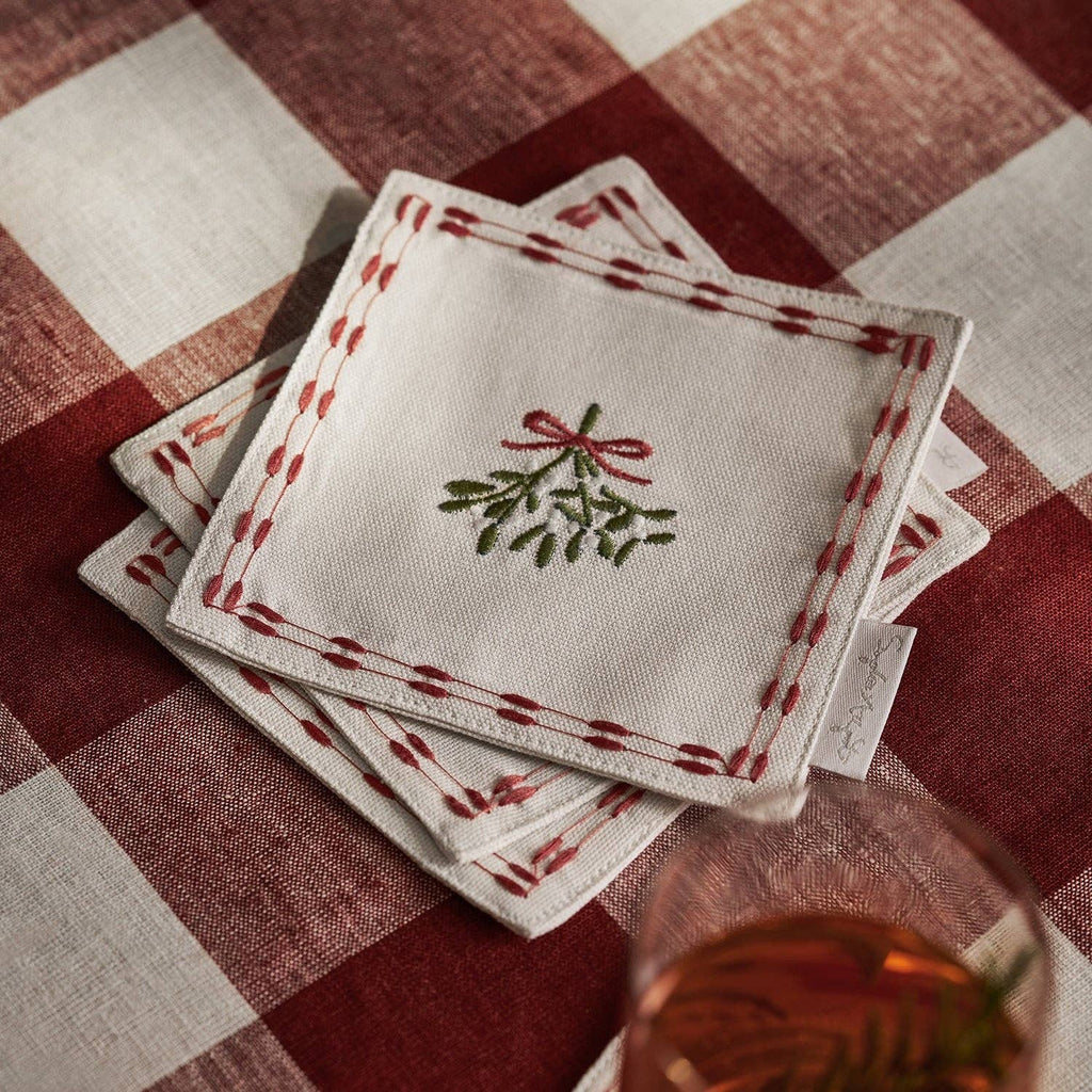 Close-up of the mistletoe embroidery and red bow on a cotton drink napkin