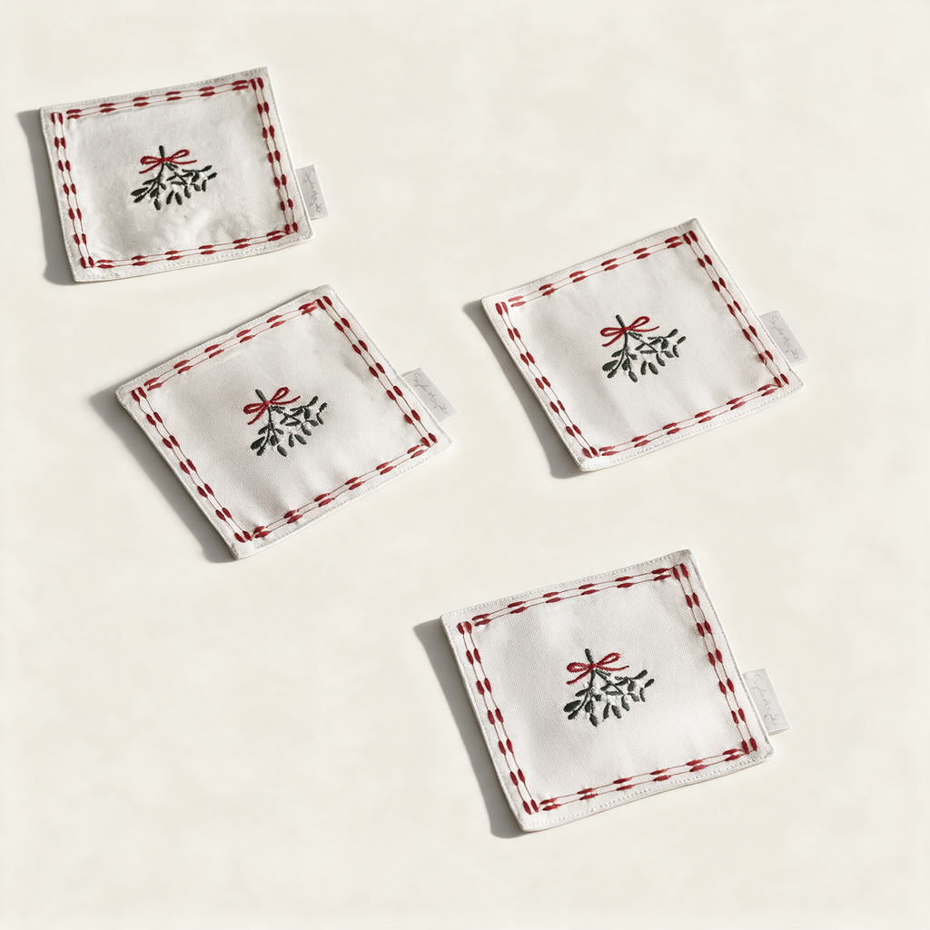 Set of four cotton mistletoe drink napkins with red bows, on a cream background