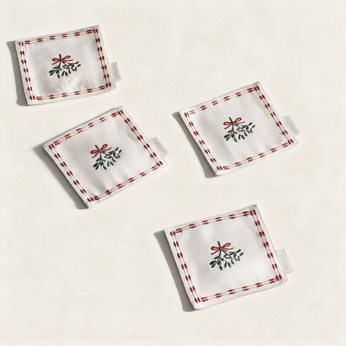 Set of four cotton mistletoe drink napkins with red bows, on a cream background