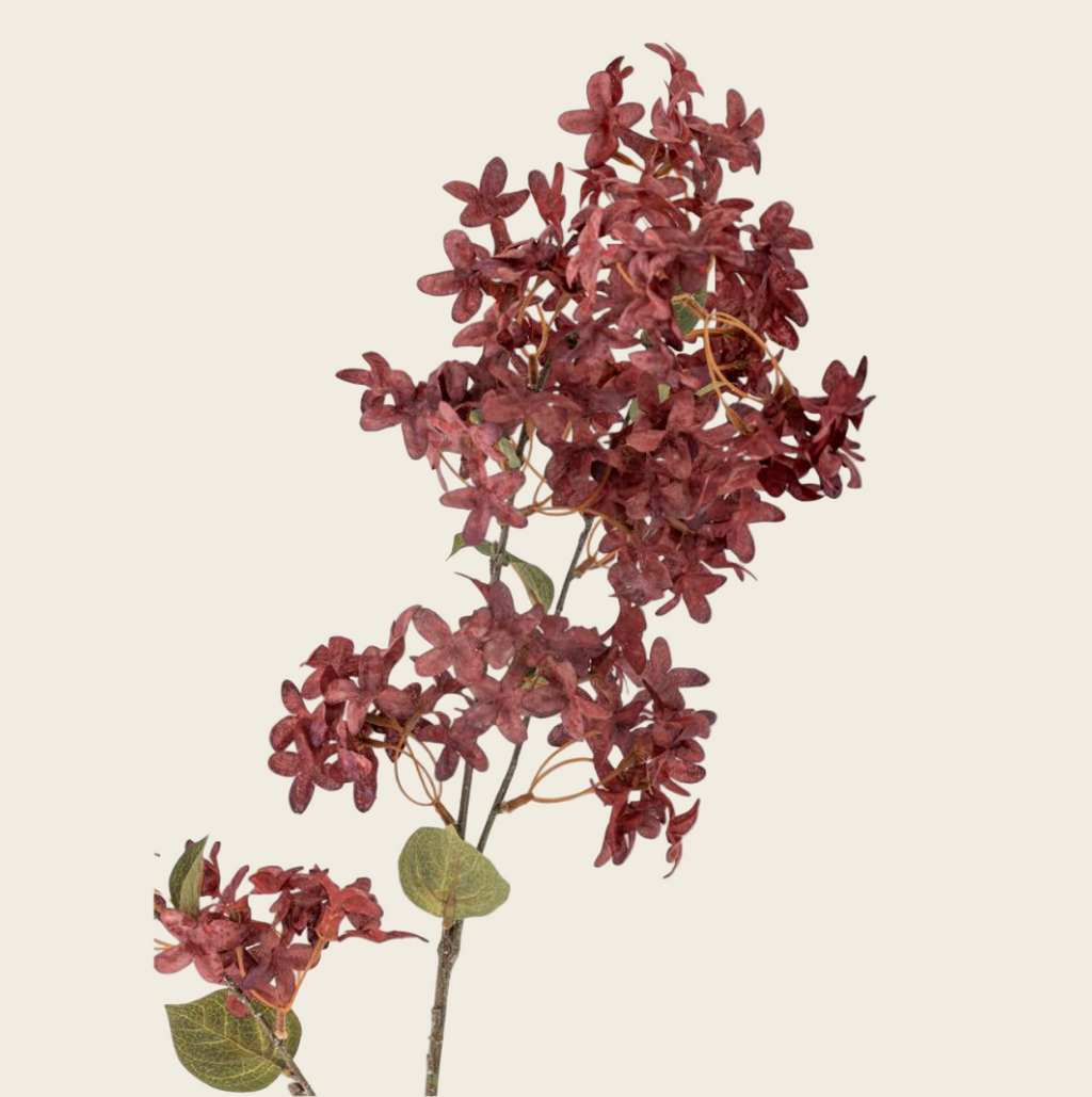 Artificial flower branch with red-brown flowers and green leaves on a white background
