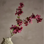Decorative vase with wavy texture holding a branch of pink flowers against a neutral background