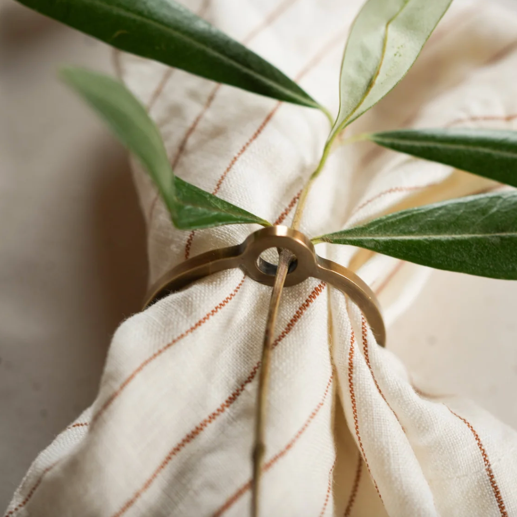 Gold napkin ring with green leaves on a striped white and brown napkin