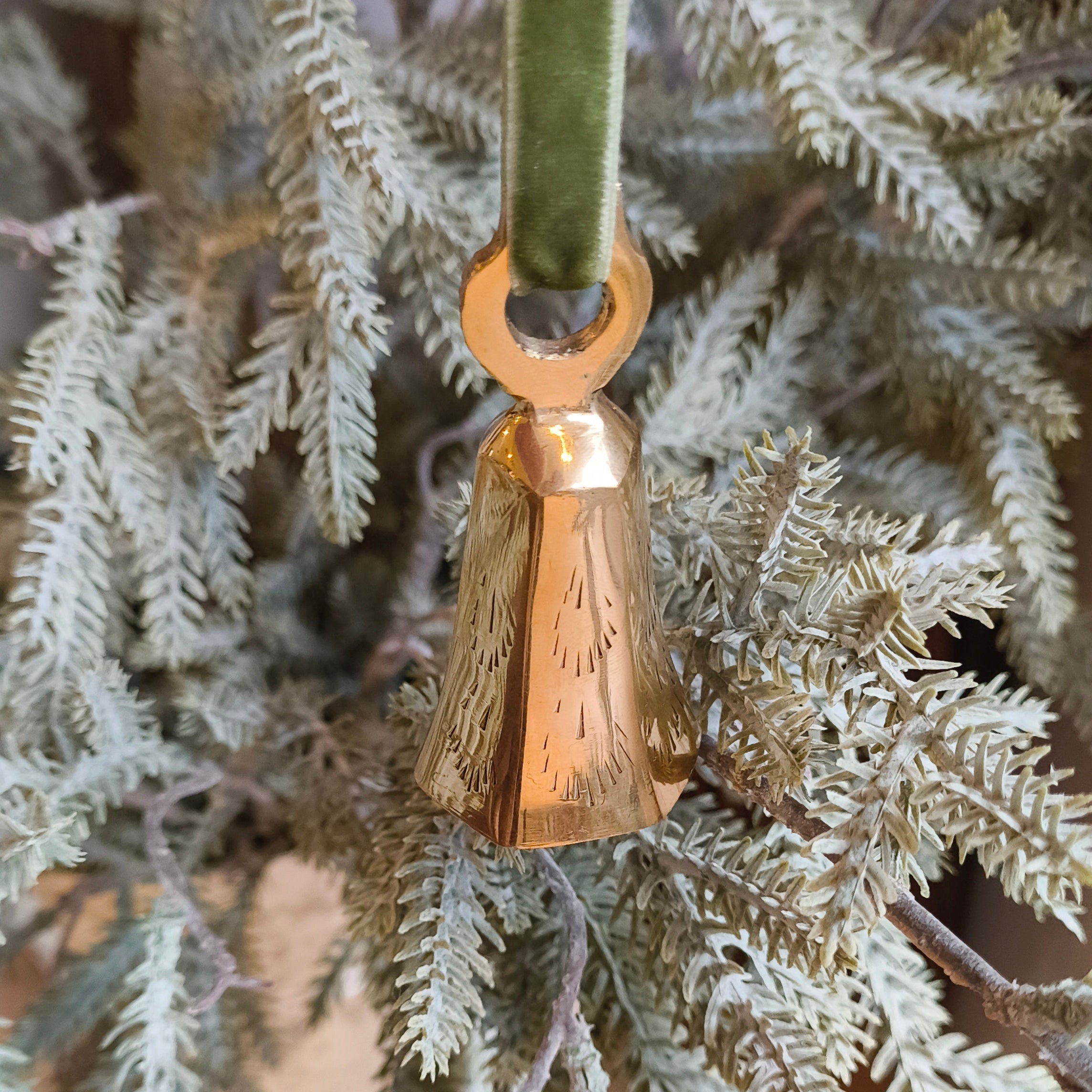 Gold bell ornament hanging on a branch of a decorated Christmas tree.