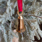 Decorative gold bell hanging from a branch of a Christmas tree with a red ribbon.