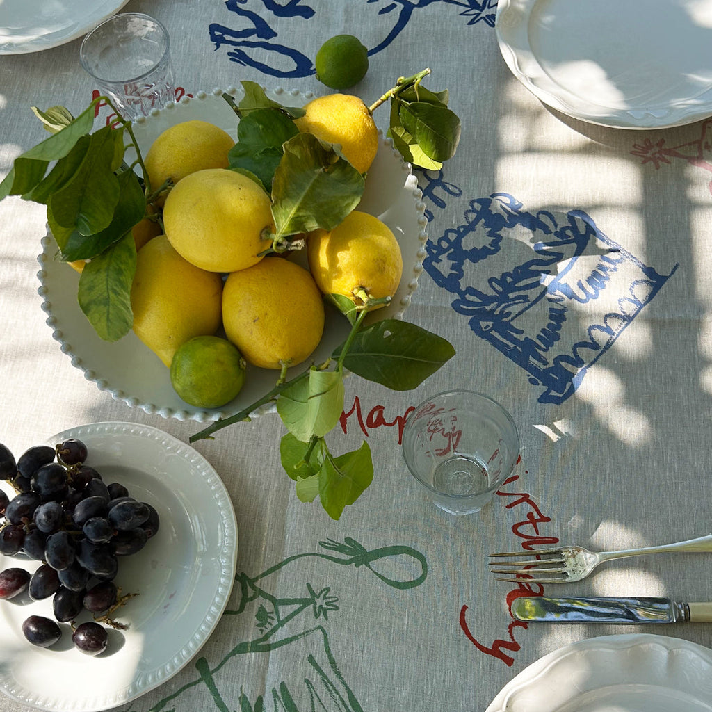 Table setting with lemons, grapes, and cutlery on a decorative tablecloth.