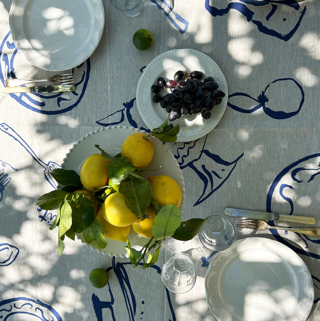 Table setting with lemons, grapes, and white plates on a decorative tablecloth.