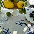 Lemons on a white pedestal dish with a blue and white tablecloth in the background