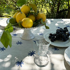 Table setting with lemons, grapes, and a glass on a tablecloth with blue star patterns.