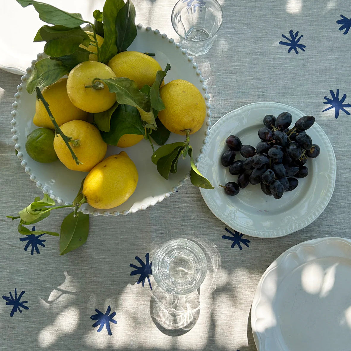 Table setting with lemons, grapes, and glasses on a tablecloth with blue star patterns.
